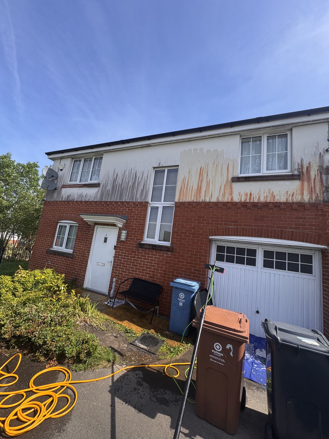 Render before cleaning — heavy orange rust streaks and black algae on white render, Oldham